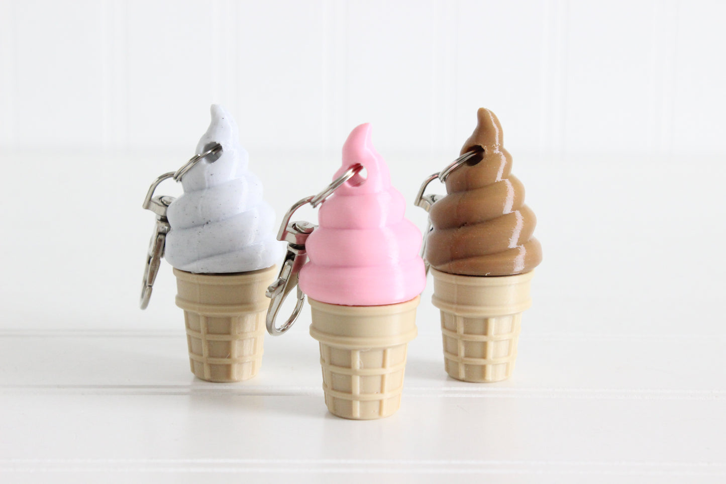Cookies-and-cream, strawberry, and chocolate swirl ice cream cone keychains displayed together.