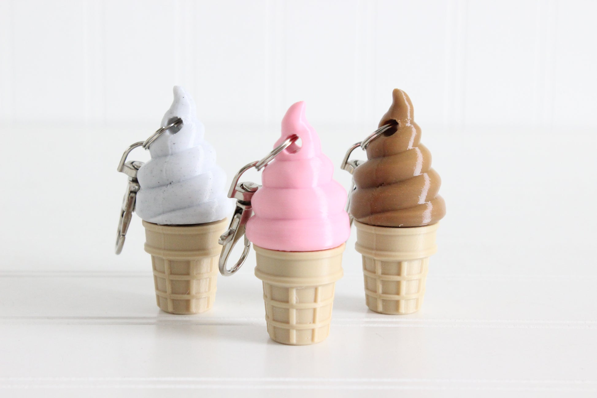Cookies-and-cream, strawberry, and chocolate swirl ice cream cone keychains displayed together.